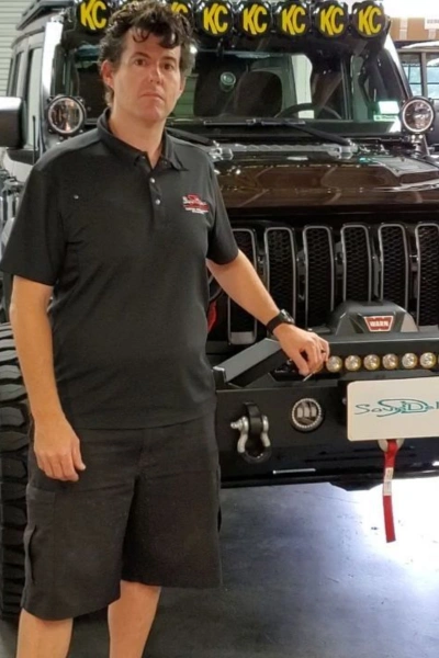 Kenny Albertini, owner of Soundelux Car Audio in San Diego, standing in front of a customized Jeep with off-road lighting and accessories.